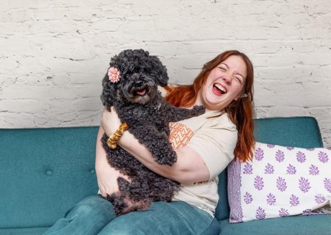 Smiling person holding a dog in their arms while on a blue couch with throw pillows
